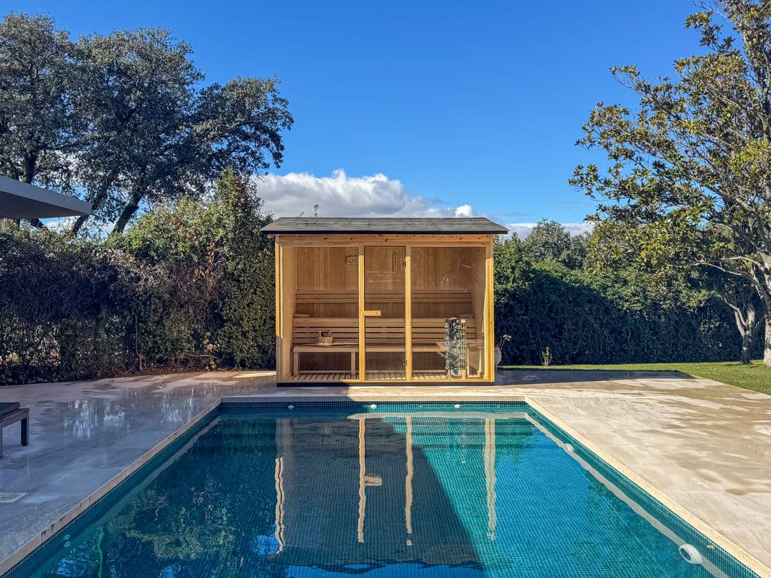 Cedar garden sauna with full-width glazing beside a swimming pool